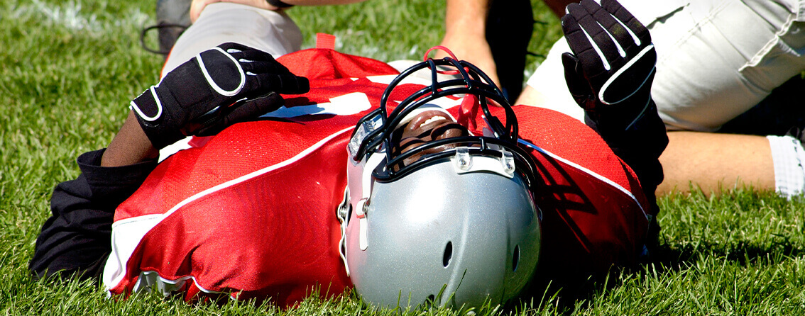 Football player on laying down on the field in pain and in need of a sports medicine doctor.